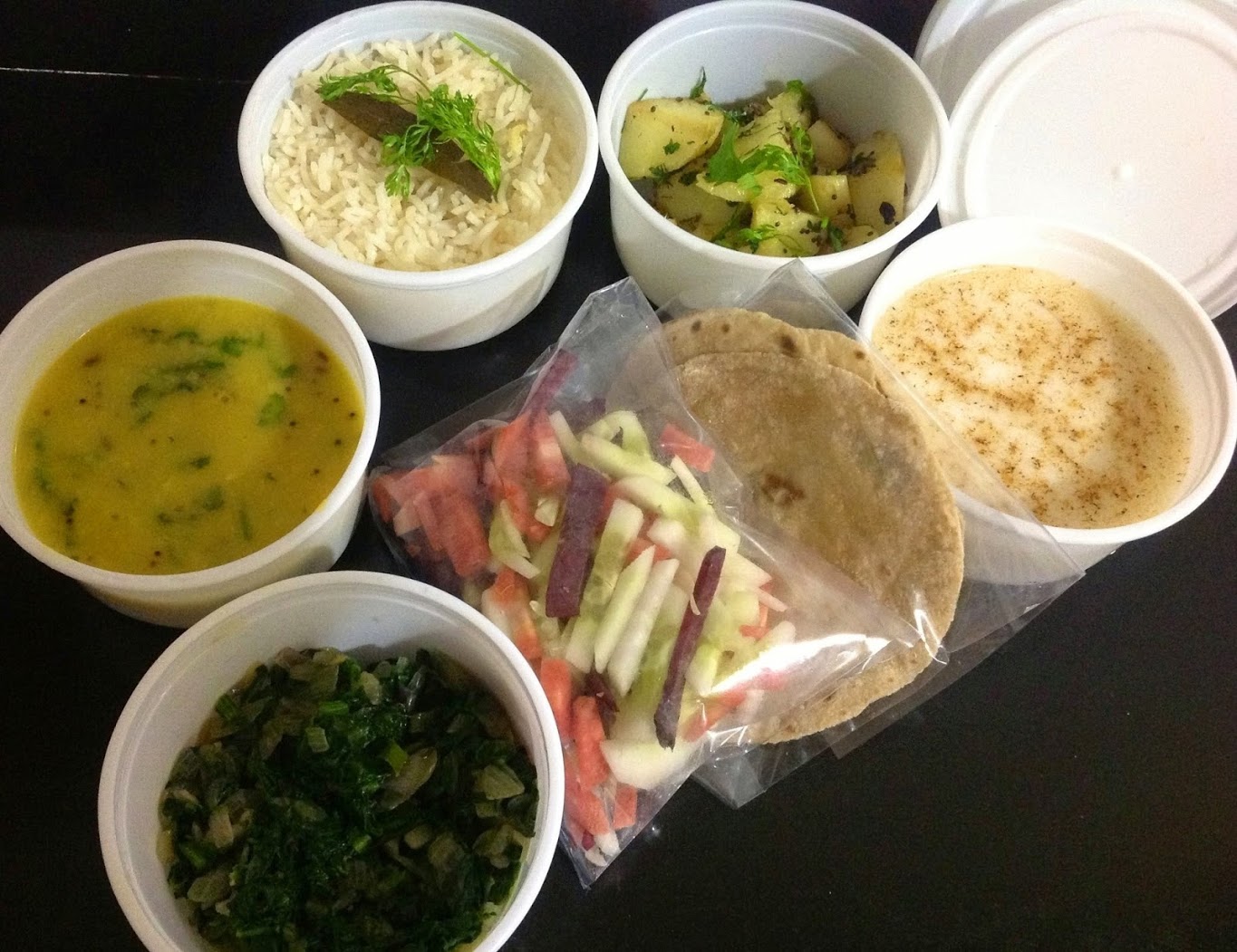 A HealthyDabba meal — bowls of dal, vegetables, sprouts, salad, raita, rotis and rice